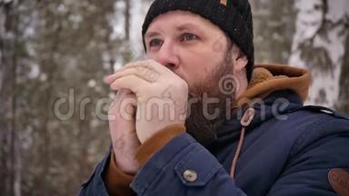 一个留着胡子的人在冬天的森林里，在他的嘴附近温暖了他的双手。 寒冷的天气。 冻僵的手。 冬季天气